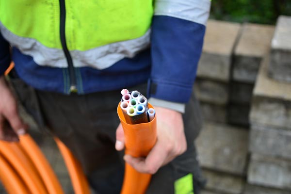 Person holding an orange conduit with multiple colored cables inside next to stacked bricks.